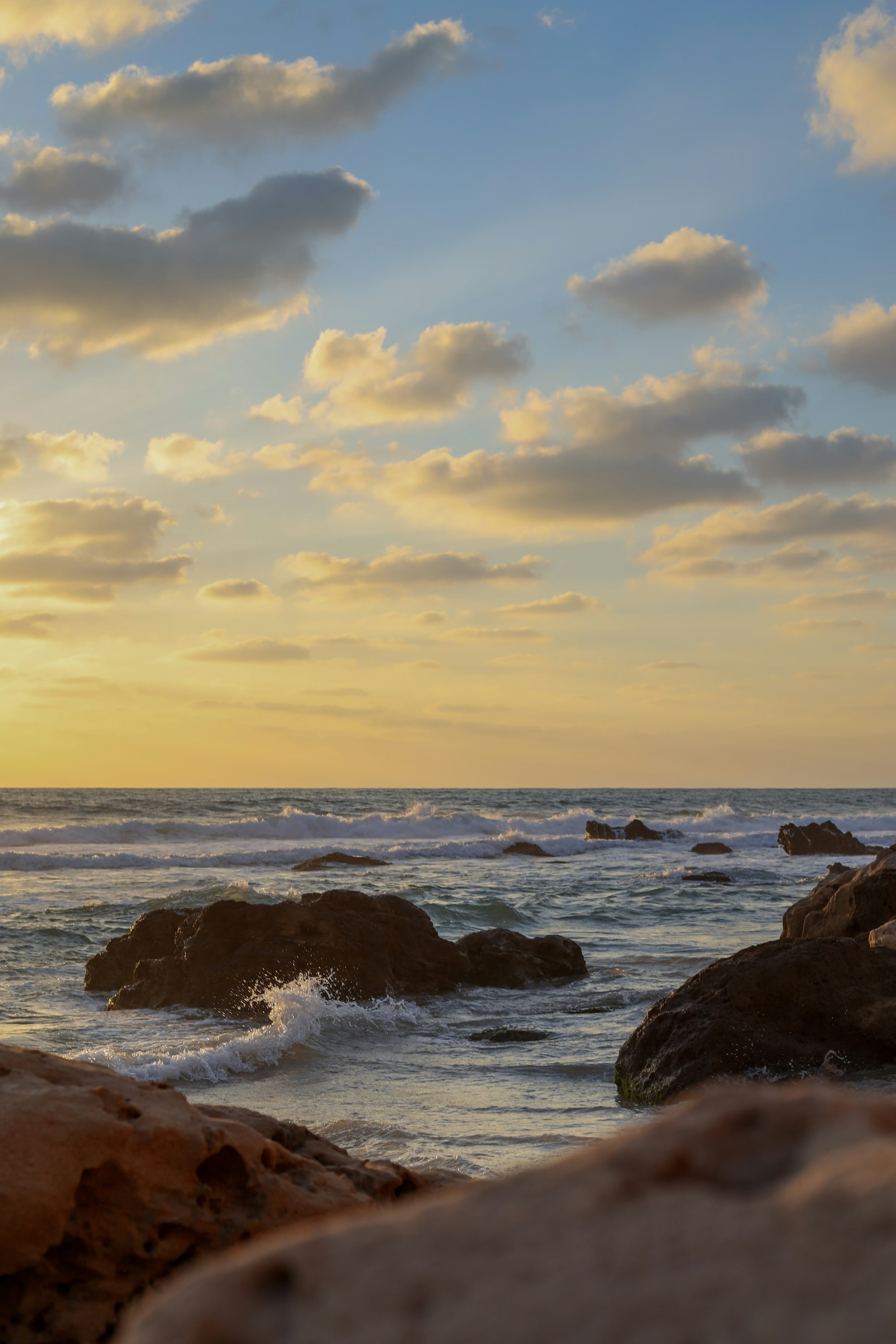Costa al atardecer, rocas y olas suaves bajo un cielo despejado